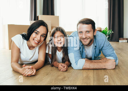 Glückliche Familie Umzug in neues Haus. Vater, Mutter und Tochter zusammen lächeln lag auf dem Boden mit Boxen auf Hintergrund Stockfoto