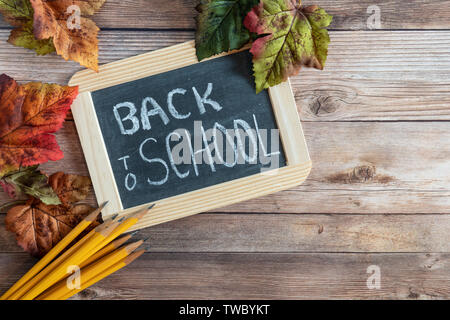 Zurück in der Schule auf einer Schiefertafel mit gelben Bleistifte und Herbstlaub auf einem Laufbelag Hintergrund gedruckt Stockfoto