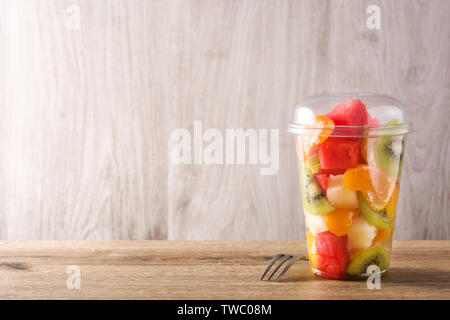 Frisches Obst in einem Plastikbecher auf hölzernen Tisch. Copyspace Stockfoto