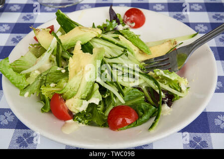 Leckere und gesunde frische Avocado und Gurke Salat mit Kirschtomaten in einer weißen Platte mit der Gabel auf einen blau-weiß karierte Tischdecke Stockfoto