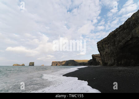 Touristische Attraktion im Süden von Island in der Nähe des Dorfes Vik. Kirkjufjara Beach in der Nähe von Kap Dyrholaey. Blick auf den berühmten Arch. Der Strand mit Bla Stockfoto