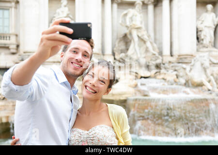 Touristische Paar auf Reisen nehmen selfie Foto vom Trevi-Brunnen in Rom, Italien. Glückliche junge romantisches Paar unterwegs in Europa, Selbstbildnis mit Smartphone Kamera. Mann und Frau glücklich zusammen Stockfoto