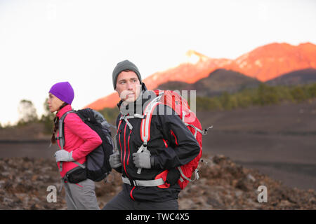 Wandern die Menschen auf den Berg. Wanderer Paar mit Rucksäcken im Freien in großer Höhe. Junger Mann, Wanderer im Fokus trekking bei Sonnenuntergang auf den Vulkan Teide, Teneriffa, Kanarische Inseln, Spanien. Stockfoto