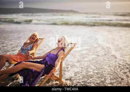 Zwei glückliche reife Frauen entspannen in Liegestühlen am Strand. Stockfoto