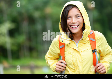 Regen Frau wandern gerne in Wald. Weibliche Wanderer portrait stehend mit Rucksack Freude an regnerischen Tag draußen tragen gelbe Regenmantel in der Natur Wald durch. Multi-ethnischen asiatisches Mädchen. Stockfoto