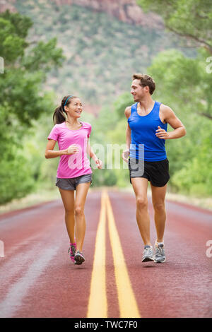 Zwei Leute joggen Fitness auf der Straße draußen in der schönen Landschaft Natur ausgeführt. Frau und Mann sport Athleten Training für Marathon. Paar zusammen, asiatische Frau, kaukasischer Mann, Stockfoto