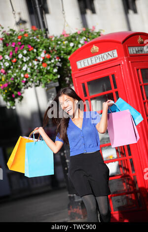 London shopper Mädchen glücklich aufgeregt Holding Einkaufstaschen durch rote Telefonzelle. Frau shopping lächelnd in London, England, Vereinigtes Königreich im Frühjahr oder Sommer. Gemischte Rasse asiatischen Kaukasischen Modell. Stockfoto