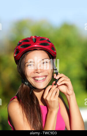 Radfahren Helm - Frau putting Fahrrad Helm außerhalb. Asiatische Mädchen auf dem Fahrrad, in der Nähe von Helm und Gesicht. Schönen gemischten Rennen Kaukasischen asiatische Frau außerhalb. Stockfoto