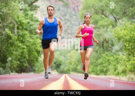 Ausführen von jungen Menschen - zwei Läufer Joggen auf der Straße in der Natur Training für Marathon laufen. Multikulturelle Paare - asiatische gemischten Rennen schönes Modell Frau und Kaukasier Männlich fitness Modell der Ausübung Stockfoto