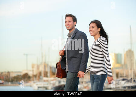 Junges Paar Walking im Freien in der Stadt alte Hafen, Port Vell in Barcelona, Katalonien, Spanien. Romantische glückliche Frau und Mann halten sich an den Händen genießen Romantik außerhalb. Interracial KAUKASISCHEN asiatischen Paar. Stockfoto