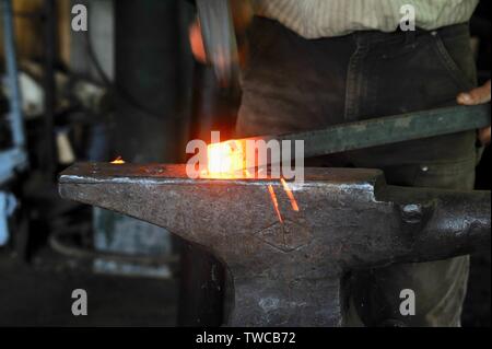 Nahaufnahme der männlichen Schmied mit Hammer schlagen red-hot Rod von Metall auf amboß Schmiede, werfen Funken während der Gestaltung Metall, Hillsboro, Wisconsin, USA. Stockfoto