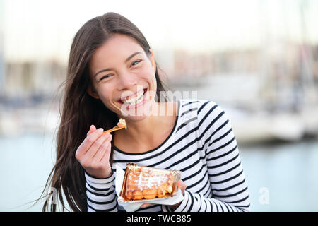 Waffeln - die Frau, die gerne im Freien essen Waffel lächelnd lachend an Kamera schaut. Schöne Mädchen essen Snack außerhalb. Stockfoto