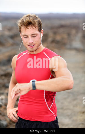 Laufender Mann in Pulsmesser GPS Uhr suchen. Runner Musik hören, Kopfhörer tragen rote Kompression t-shirt Top. Stockfoto