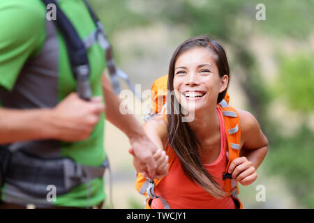 Helfende Hand - Wandern Frau Hilfe auf Wanderung glücklich lächelnd Hindernis zu überwinden. Aktiver Lebensstil Wanderer Paar reisen. Schönen Lächeln gemischten Rennen asiatischen Kaukasischen weibliche Modell. Stockfoto