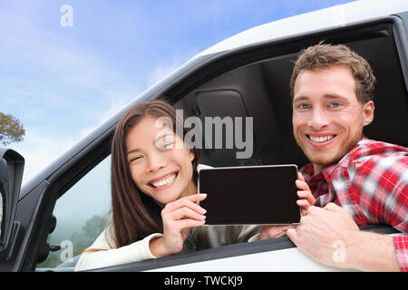 Tablet PC - Paar fahren im Auto mit Bildschirm mit App oder Nachricht. Junge glücklich Treiber auf Road Trip. Asiatische Frau, kaukasische Mann. Stockfoto