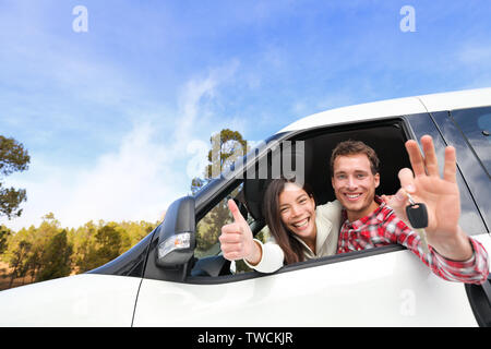 Neues Auto - glückliches Paar anzeigen Autoschlüssel fahren Spaß auf Straße Reise Fahrt im Mietwagen. Glücklich Lifestyle mit schönen jungen interracial Paare im Freien auf Reisen. Mann und Frau Passagier. Stockfoto