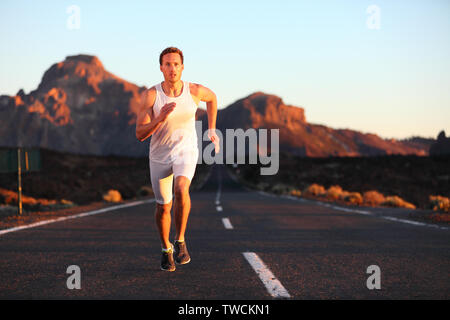 Athleten laufen sprintet bei Sonnenuntergang auf der Straße. Männliche Läufer Ausbildung in der Berglandschaft in der Nacht. Passen junge muskulöse Fitness Sport Modell in seiner 20. Stockfoto