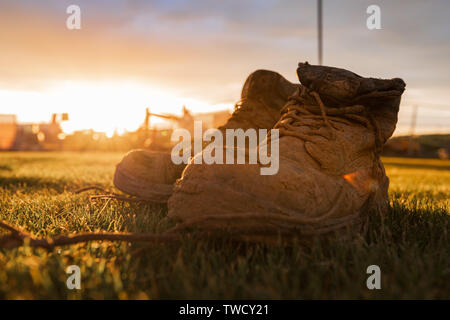 Sicherheitsstiefel auf einer Baustelle im Schlamm, die vor einem hellen Sonnenuntergang abgedeckt Stockfoto