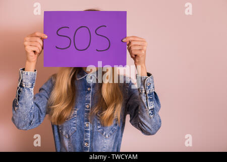 Frau mit Papier mit Word SOS beim Stehen vor der Wand. Stockfoto