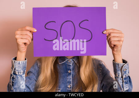 Frau mit Papier mit Word SOS beim Stehen vor der Wand. Stockfoto