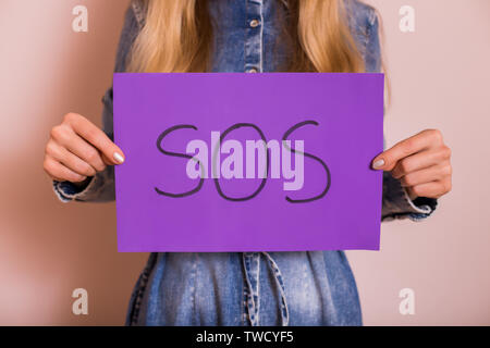 Frau mit Papier mit Word SOS beim Stehen vor der Wand. Stockfoto