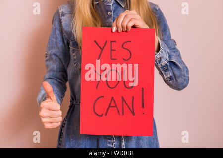 Frau mit Papier mit Text ja Sie können und Daumen oben beim Stehen vor der Wand. Stockfoto