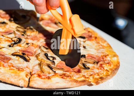 Close up Messer schneiden Pizza mit Salami, Pilzen und Käse aus der Nähe Stockfoto