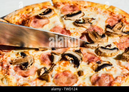 Close up Messer schneiden Pizza mit Salami, Pilzen und Käse aus der Nähe Stockfoto