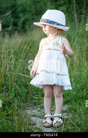 Kleinkind Mädchen in einem wunderschönen weißen Kleid und lustig einen großen Hut Stockfoto