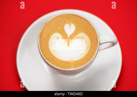 Blick von oben auf die Kaffeetasse mit Latte Art auf rotem Hintergrund. Stockfoto