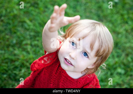 Wenig kaukasische Mädchen anspruchsvolle Gesicht und Hand closeup Draufsicht auf grünem Gras Hintergrund Stockfoto