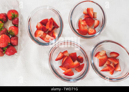 In Scheiben geschnittene Erdbeeren in klarem Glas Schalen, in Scheiben geschnittene Erdbeeren auf einem Schneidebrett, Obst, Salat, Dessert Stockfoto