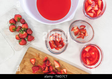 Strawberry Jelly Vorbereitung. In Scheiben geschnittene Erdbeeren in klarem Glas Schalen, in Scheiben geschnittene Erdbeeren auf einem Schneidebrett, Obst, Salat, Dessert, Gelee Stockfoto