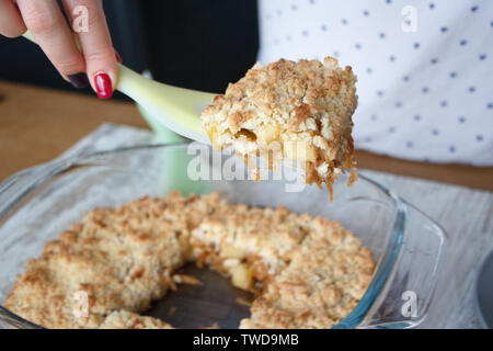 Weibliche Hände nehmen ein Stück Apfel knackig frisch gebackene hausgemachte Kuchen aus einem Glas Schimmel auf einem Teller, Copyspace Stockfoto