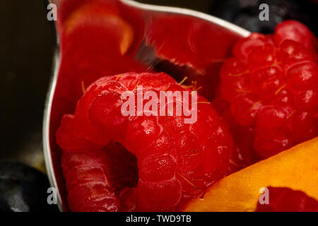 Makro einer Glas Schale mit Früchten mit einem Löffel und verschiedene Früchte. Der primäre Rahmen ist meistens die Himbeeren in den Löffel in der Nähe Makrobereich. Stockfoto