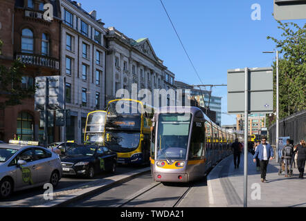 Sommer Abend in Dublin, mit Menschen zu Fuß entlang einer belebten Dubliner Straße wie der Verkehr in Eden Quay und eine Straßenbahn LUAS wartet, um fortzufahren. Stockfoto