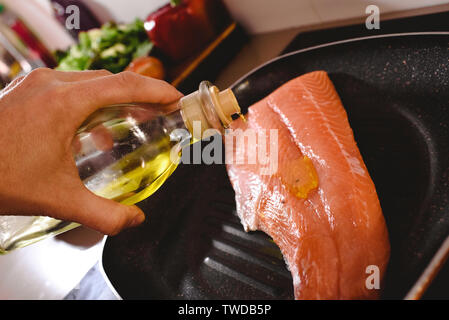 Roher Lachs filet in der Pfanne kochen gießen Olivenöl über es, um es zu kochen. Stockfoto
