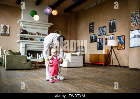 Glücklicher Vater führt eine einjährige Tochter an der Hand In einem gemütlichen Zuhause Stockfoto
