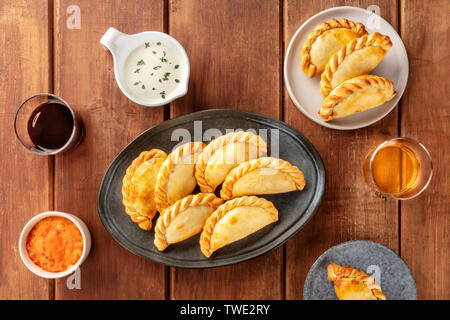Empanadas mit Saucen und Wein, geschossen von oben auf einen dunklen Holzmöbeln im Landhausstil Hintergrund Stockfoto