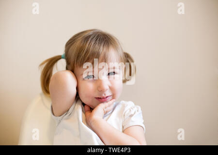 Wenig sly kid Kaukasischen girl cute Nahaufnahme Gesicht Porträt mit Pigtails auf einfachen Hintergrund Stockfoto