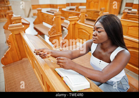 Afrikanische amerikanische Frau in der Kirche zu beten. Gläubige meditiert, in der Kathedrale und spirituelle Zeit des Gebets. Afro girl halten Sie rosenkranz und Bibel während Stockfoto