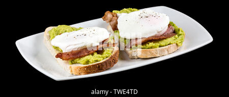 Avocado Toast überbacken mit Speckscheiben und 2 pochierte Eier mit Reflexion auf schwarzem Hintergrund isoliert. Studio Shot Stockfoto