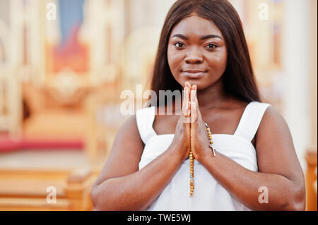 Afrikanische amerikanische Frau in der Kirche zu beten. Gläubige meditiert, in der Kathedrale und spirituelle Zeit des Gebets. Afro girl gefalteten Händen mit Rosenkranz. Stockfoto