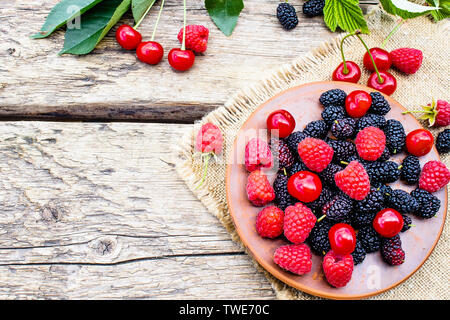 Saftige frische und köstliche Beeren, Kirschen, Himbeeren, Maulbeeren in einer Schüssel auf Holz- Hintergrund. Close-up Stockfoto