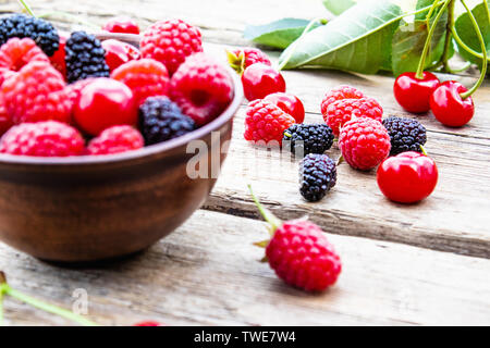 Saftige frische und köstliche Beeren, Kirschen, Himbeeren, Maulbeeren in einer Schüssel auf Holz- Hintergrund. Close-up Stockfoto