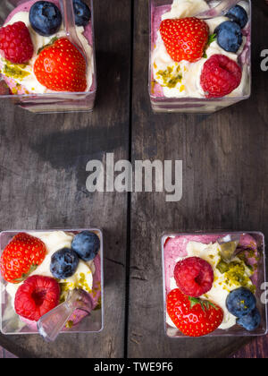 Tassen Himbeeren Brombeeren Erdbeeren serviert mit Nüssen und Sahne über alten Holztisch. Ansicht von oben. Quadratisches Bild Stockfoto