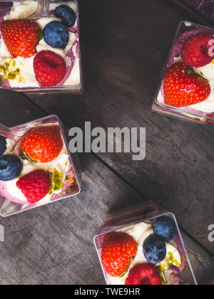 Tassen Himbeeren Brombeeren Erdbeeren serviert mit Nüssen und Sahne über alten Holztisch. Ansicht von oben. Quadratisches Bild Stockfoto