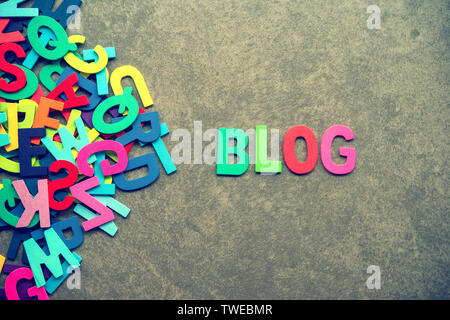Die bunten Worten "BLOG" mit Holz Buchstaben neben einem Stapel der anderen Buchstaben auf grauem Hintergrund. Stockfoto