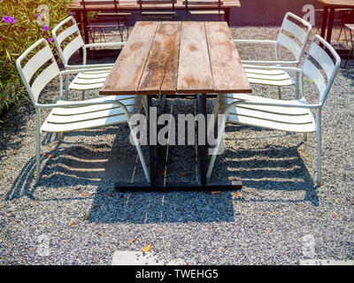 Alte Holz Esstisch und vier weißen Stahl Sesseln auf Kiesboden. Stockfoto