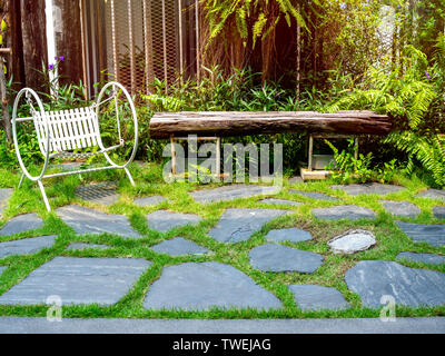 White vintage Garten Hollywoodschaukel auf Steinboden im grünen Garten mit Sonnenschein. Stockfoto